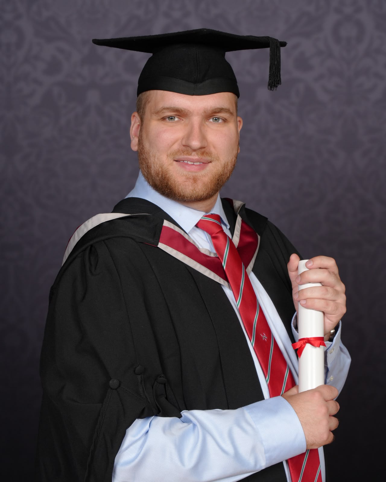 Ryan Smith in graduation robes holding a degree scroll.